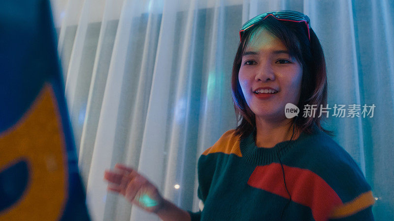 年轻的亚洲女dj女孩玩音乐和抓挠轨道专业dj midi控制器在彩色的房子聚会在晚上。多元文化的朋友在大学宿舍聚会上玩得很开心。